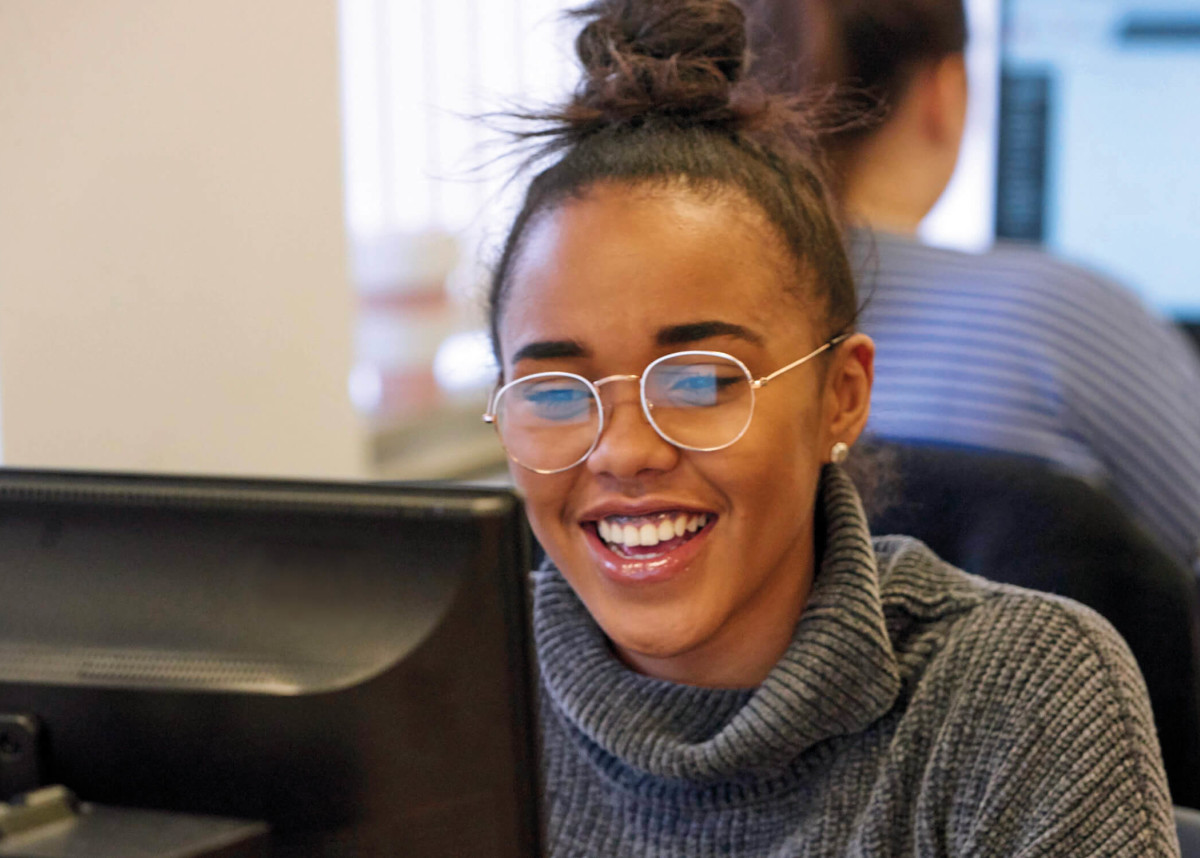 An Access to Higher Education student smiling, sat at their computer.