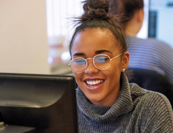 An Access to Higher Education student smiling, sat at their computer.