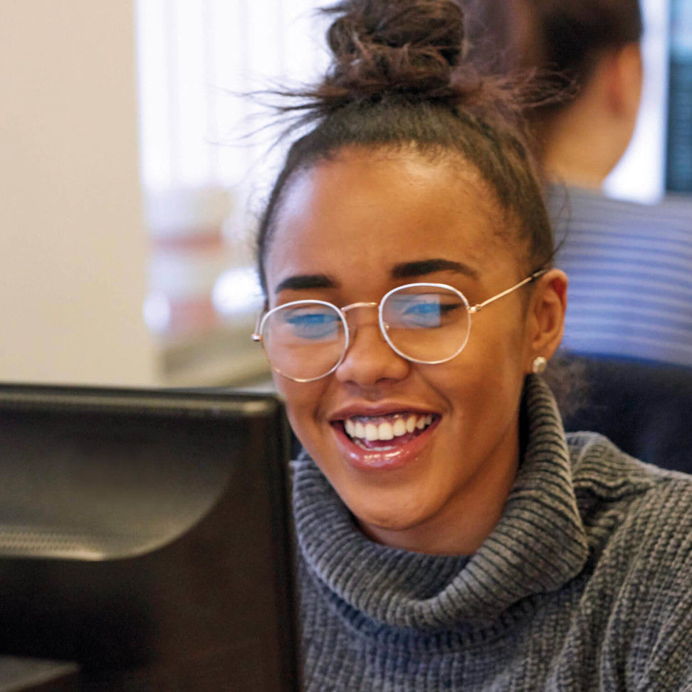 An Access to Higher Education student smiling, sat at their computer.